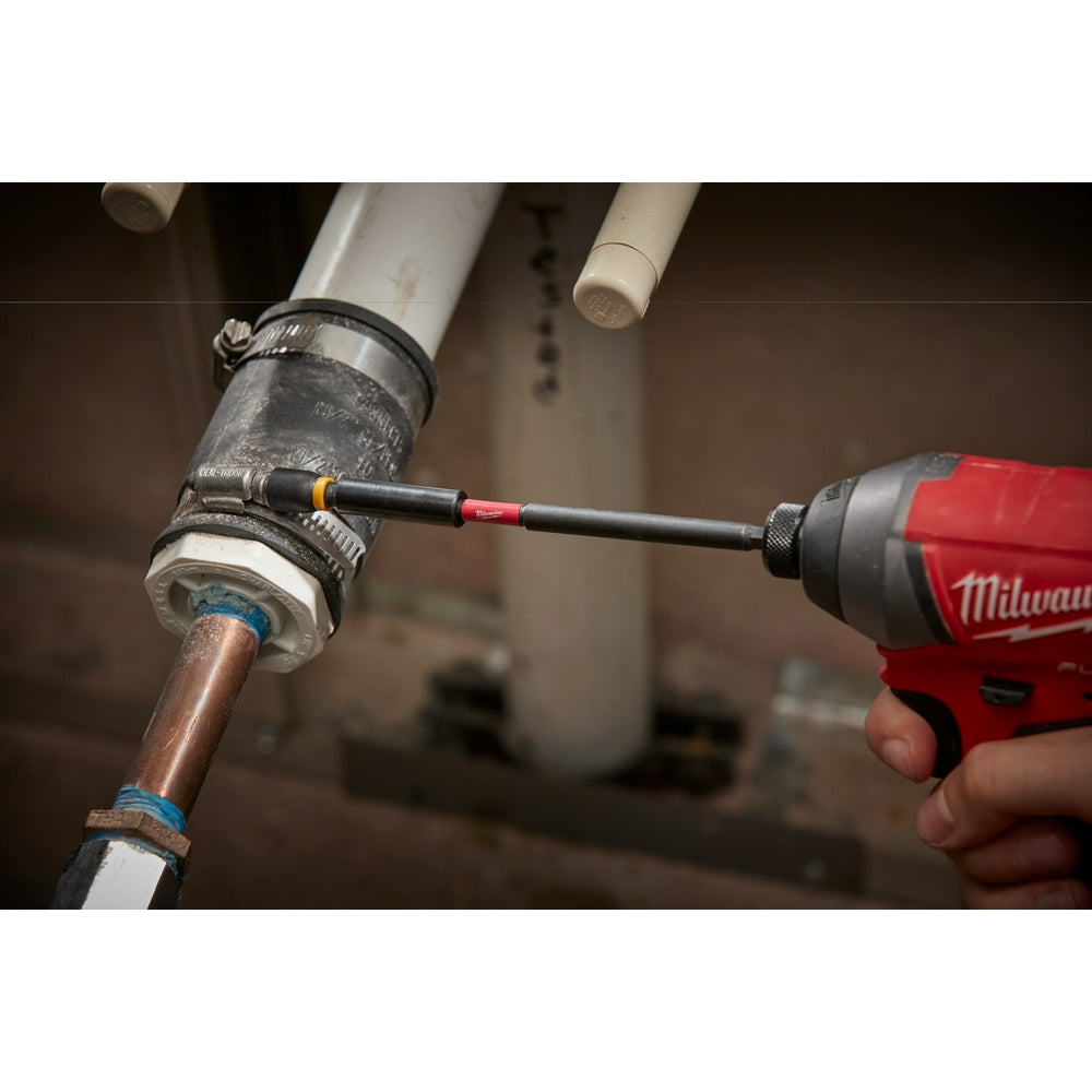 Black and red magnetic bit holder inserted into Milwaukee drill, positioned against copper pipe fitting on job site.
