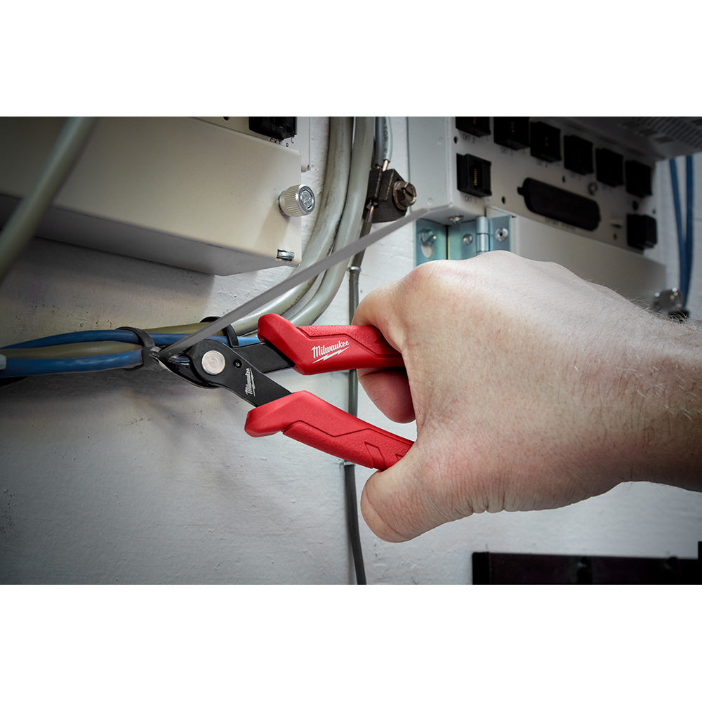 Hand holding Milwaukee mini flush cutters with red handles cutting electrical wire.