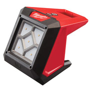 Milwaukee M12 compact flood light with red and black housing, LED grid front panel, and black rubber base.