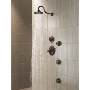 Stainless steel shower head with curved arm mounted on tiled bathroom wall, water streaming downward.