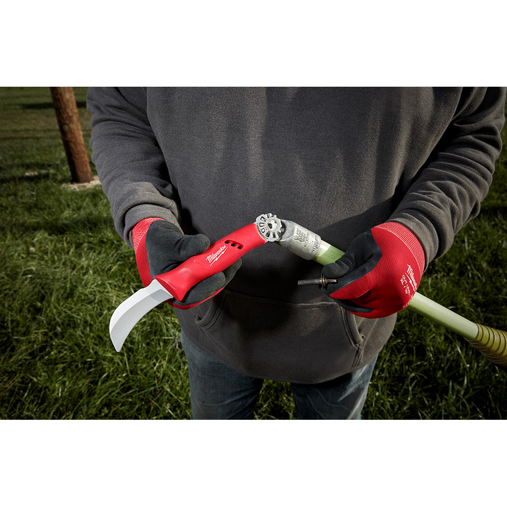 Milwaukee lineman's hawkbill knife with red handle and silver blade held in gloved hands outdoors.