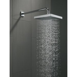 Stainless steel square raincan shower head with wall-mounted arm dispensing water against dark tile background.