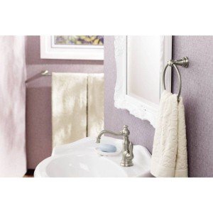 Brushed nickel single-handle bathroom sink faucet with curved spout installed on white pedestal sink.