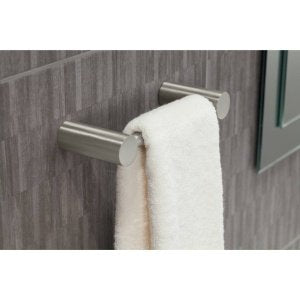 Brushed nickel towel bar mounted on gray tile wall with white towel draped over it.