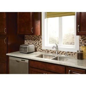 Chrome kitchen faucet with high arc spout and single handle mounted on white countertop above double sink.