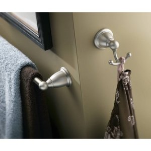 Brushed nickel double robe hook mounted on beige wall with towel and accessories hanging.
