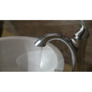 Brushed nickel single-handle bathroom faucet with curved spout positioned over white sink basin.