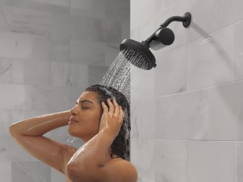 Matte black shower filter head mounted on bathroom wall with water streaming down during use.