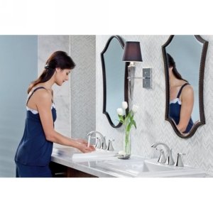 Oil rubbed bronze two-handle bathroom sink faucet with widespread trim kit installed on white sink with decorative mirrors.