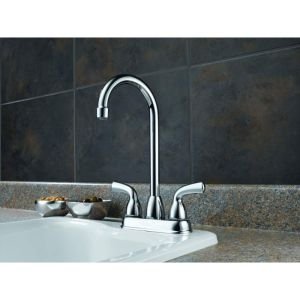 Chrome bar faucet with dual handles and curved spout over white sink.