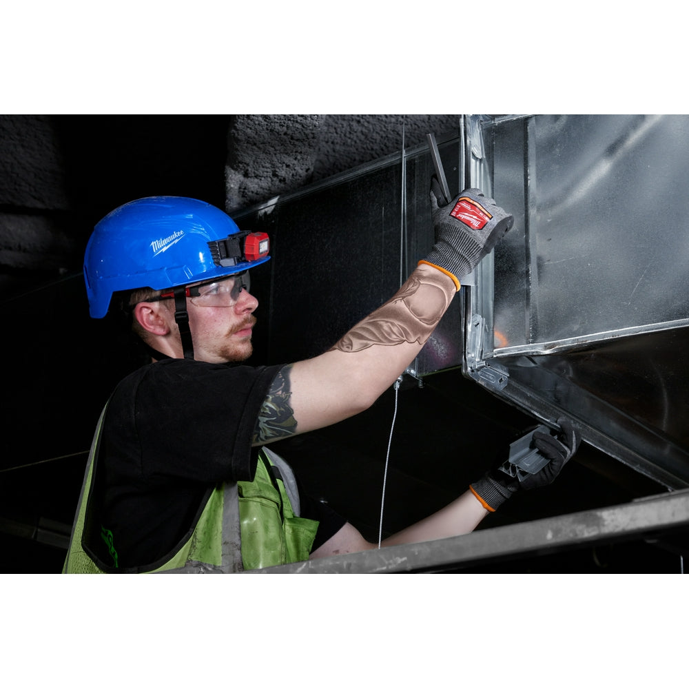 Worker wearing tan and black nitrile dipped gloves with orange trim while handling metal equipment.