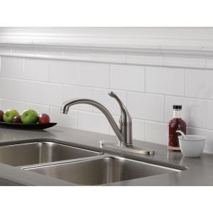 Chrome single handle kitchen faucet with curved spout mounted on stainless steel sink.