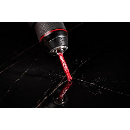 Diamond grit hole saw with red cutting head attached to power drill, cutting through black material.