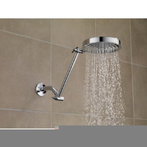 Chrome adjustable shower arm with round rain showerhead mounted on beige tile wall with water flowing.