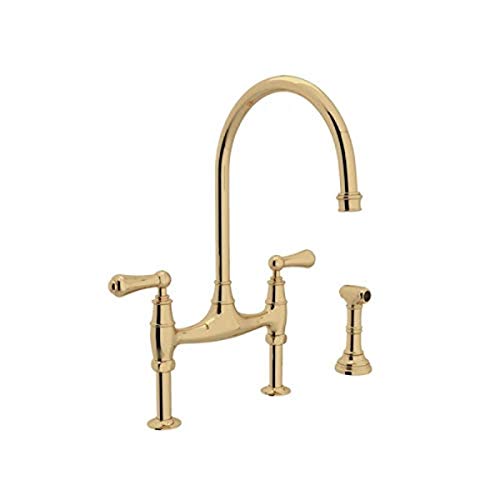 Unlacquered brass bridge kitchen faucet with high arched spout, dual handles, and separate side spray attachment.