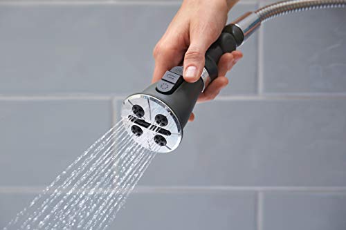 Hand holding chrome shower head with black grip and multiple spray settings against tiled bathroom wall.