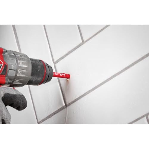 Red and black drill with diamond grit hole saw bit drilling into white tile surface.