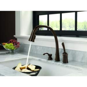 Champagne bronze kitchen faucet with curved spout and soap dispenser pump on marble countertop.