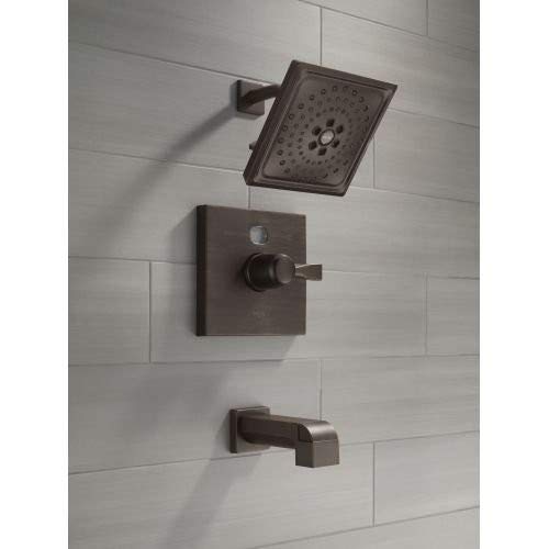 Venetian bronze shower trim set with square showerhead, control valve, and tub spout mounted on white tile wall.