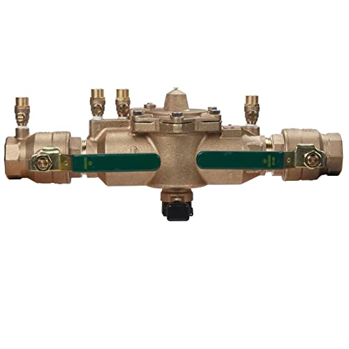 Brass backflow preventer with two green lever handles, threaded ports on sides, and relief valve outlet on bottom.