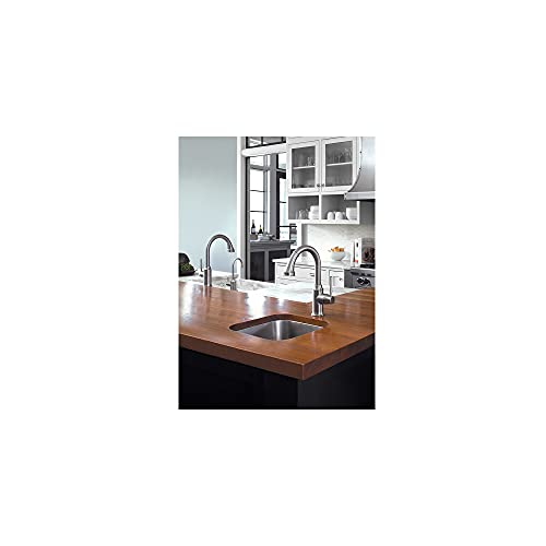 Chrome bar faucet with curved spout installed over kitchen sink with wooden countertop.