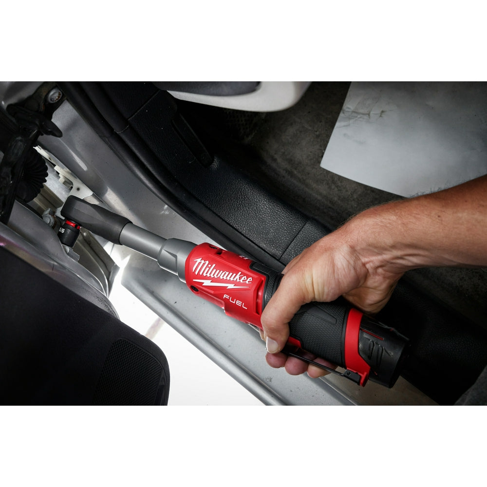 Red and black Milwaukee M12 FUEL ratchet with protective boot held in hand over car door frame.