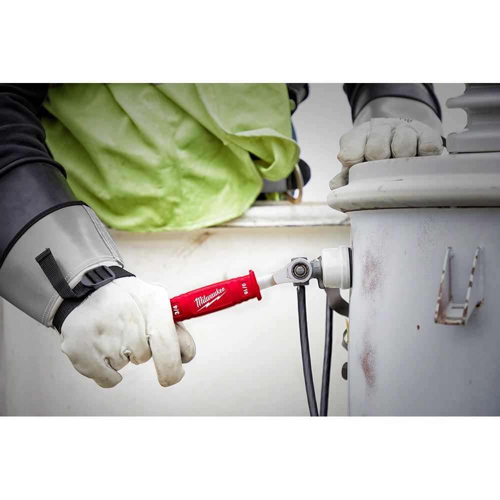 Worker in insulated gloves holding red Milwaukee ratcheting wrench connected to electrical equipment.
