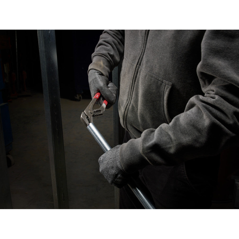 Person in work gloves holding a 12-inch straight jaw pliers with red grip accents against a metal surface.