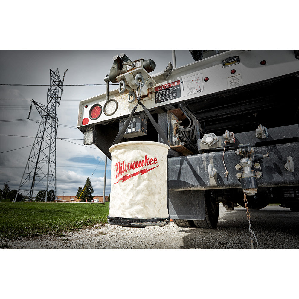 White canvas utility bucket with red Milwaukee logo sitting beside industrial equipment.