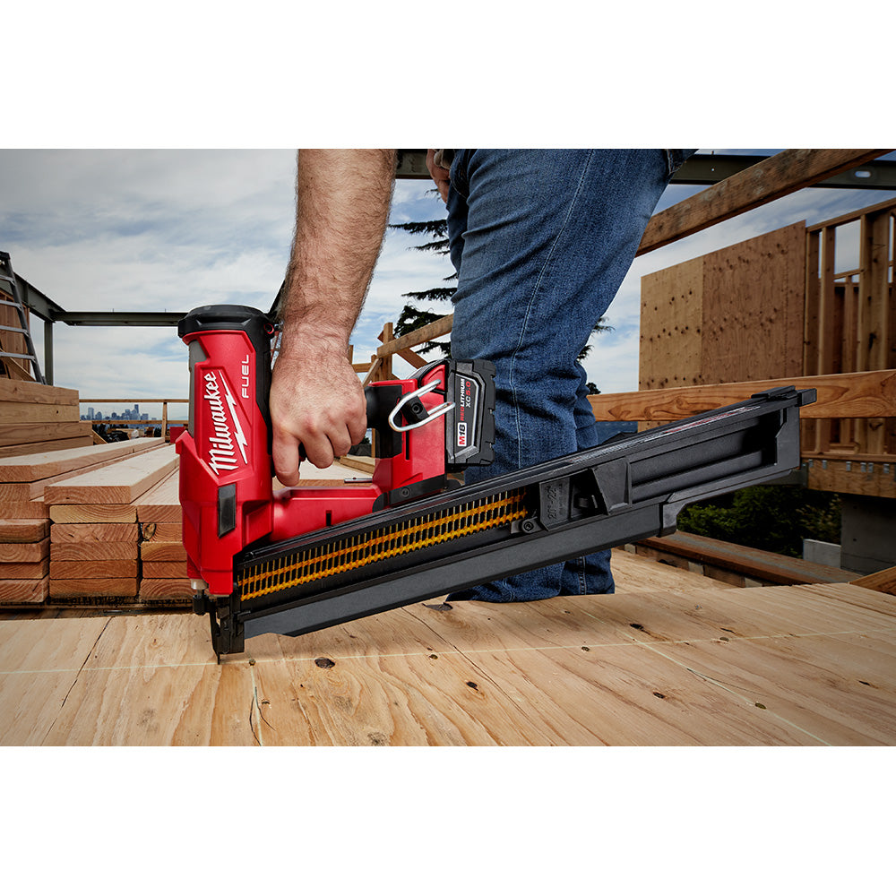 Red Milwaukee M18 FUEL framing nailer with black extended magazine being held by a person on wooden decking.