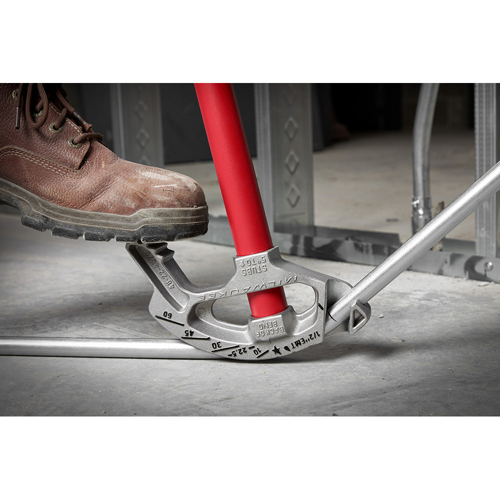 Milwaukee aluminum conduit bender with red handle being used on concrete surface with work boot visible.