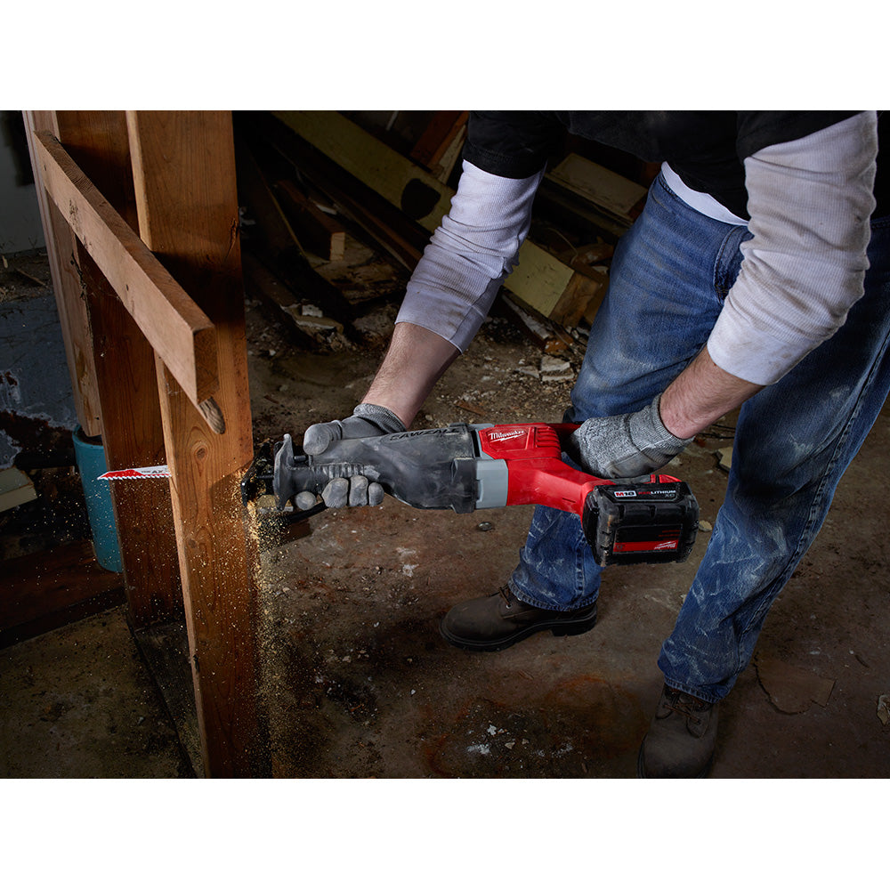 Milwaukee M18 reciprocating saw with red and black housing held by gloved hand cutting wood framing.