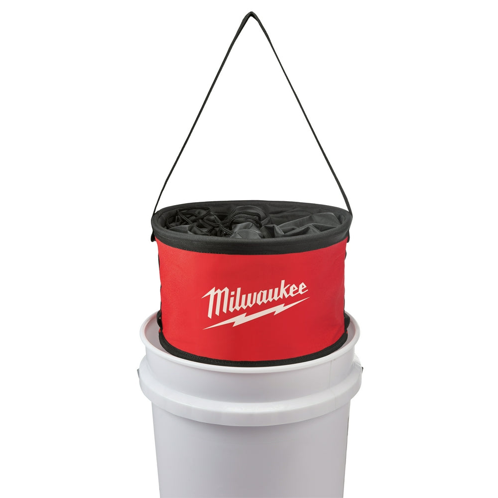 Red and black cylindrical organizer bag with black shoulder strap and compartmented interior, suspended above white bucket.