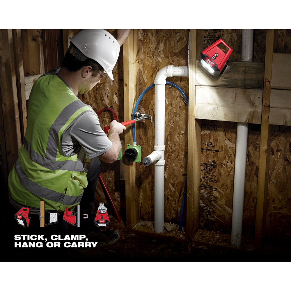 Red and black Milwaukee M12 flood light mounted on white pipe, illuminating work area in construction setting.