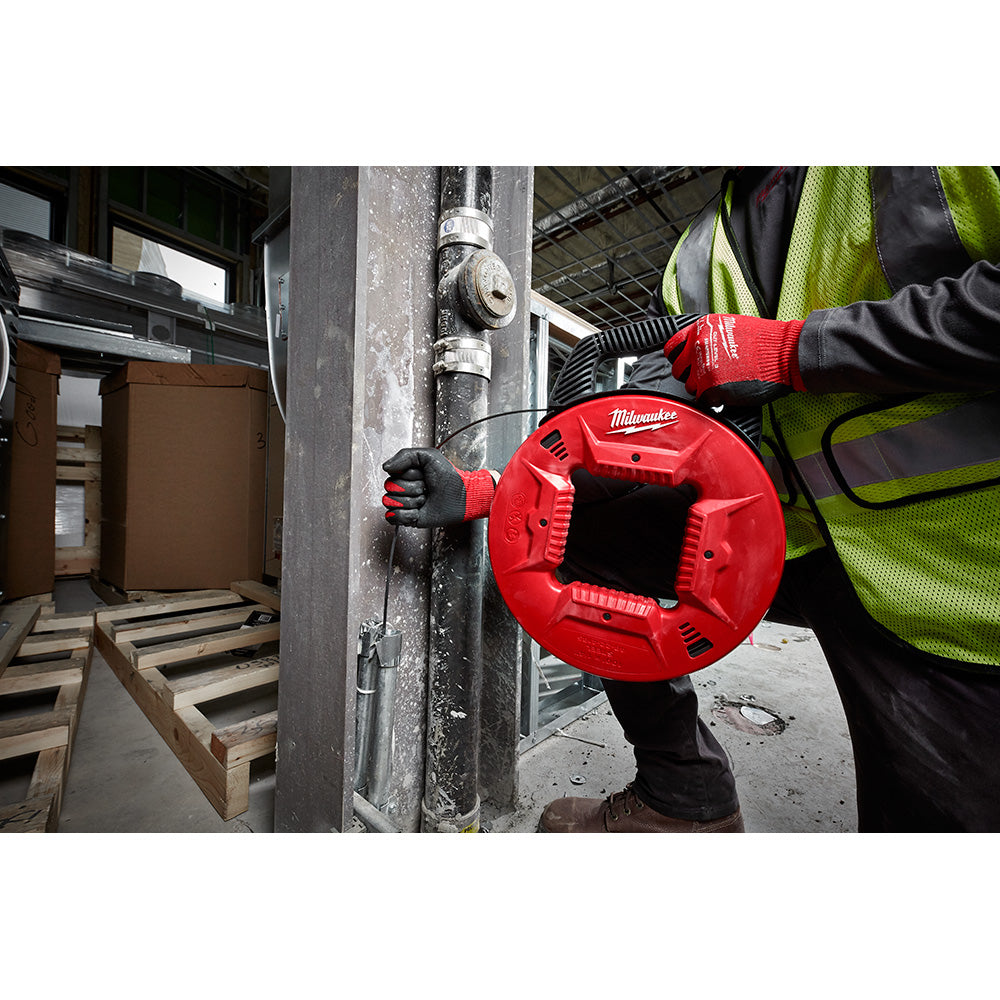 Milwaukee red steel fish tape reel being held by worker in safety gear on construction site.