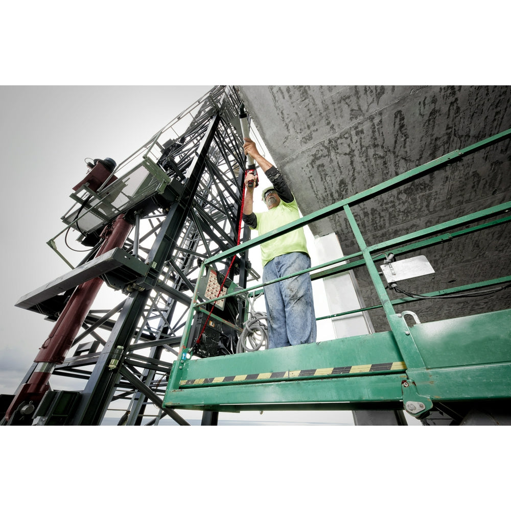 Worker in safety vest and harness secured by red locking lanyard while working at height on industrial structure.