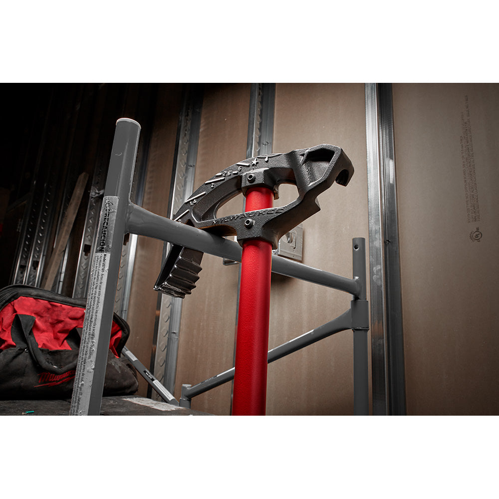 Black iron conduit bender with red handle and base mounted on work stand with metal framing.