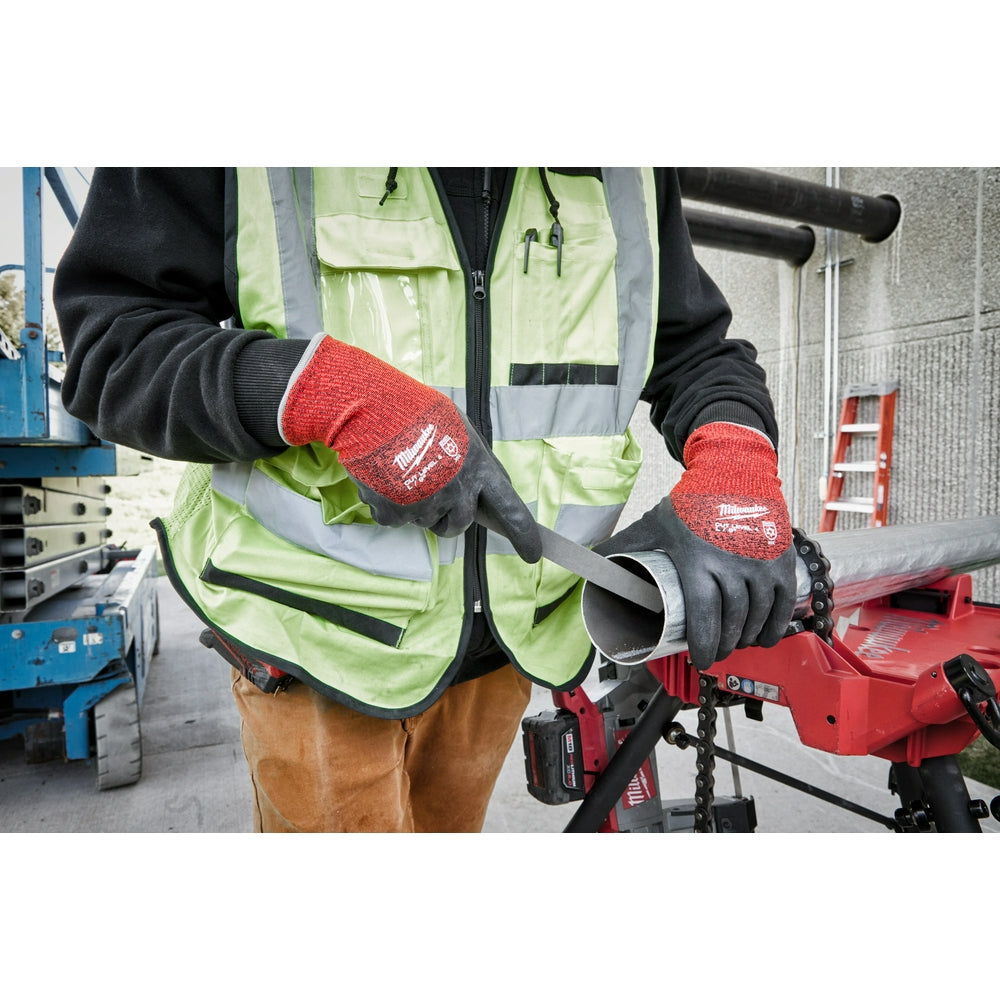 Red and black dipped work gloves worn on hands holding a metal pipe in an industrial setting.