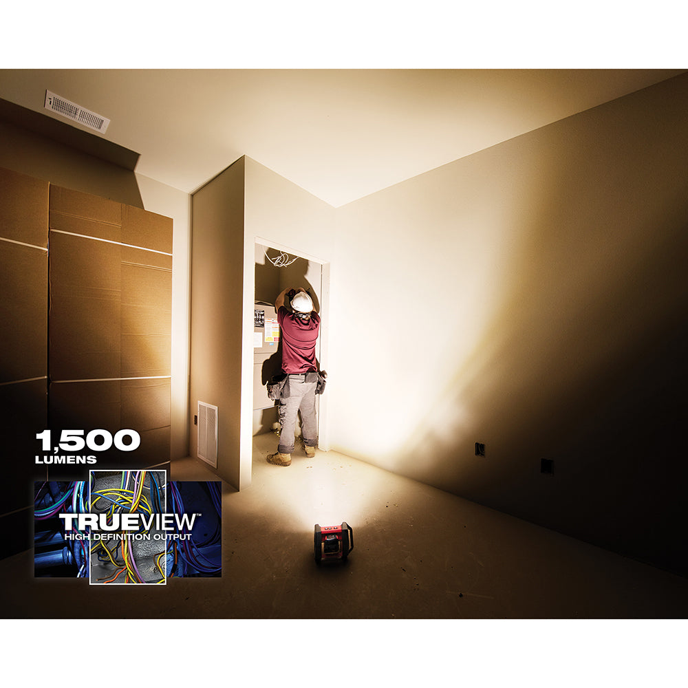 Red and black Milwaukee M18 LED flood light illuminating an interior room with warm white light.