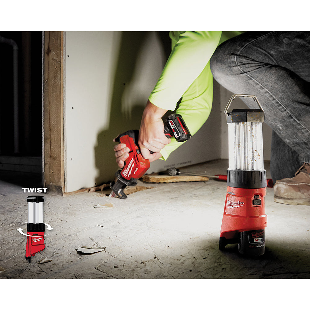 Red and black cordless LED lantern with cylindrical white light diffuser, shown in two sizes on a construction site floor.