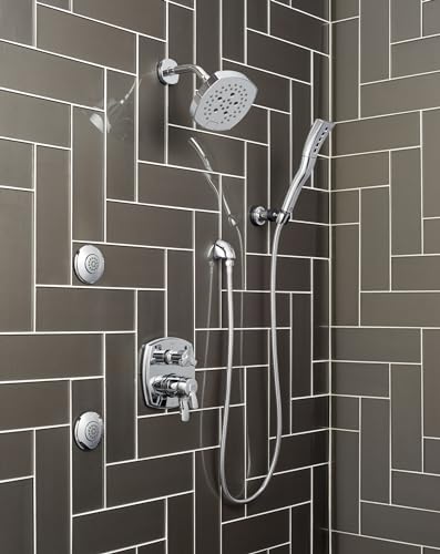 Chrome shower system with overhead rainfall showerhead, handheld wand, and body jets mounted on dark subway tile wall.