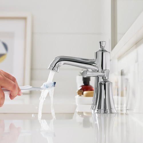 Polished nickel widespread bathroom faucet with single tall spout and handle, water flowing from spout over white sink.