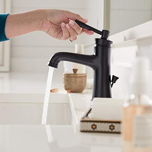 Matte black single-hole faucet with curved spout and lever handle, shown with water running and hand operating pull-down spra