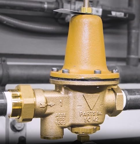 Brass RPZ backflow preventer with yellow bonnet, threaded connections, and inlet/outlet ports on gray pipe background.
