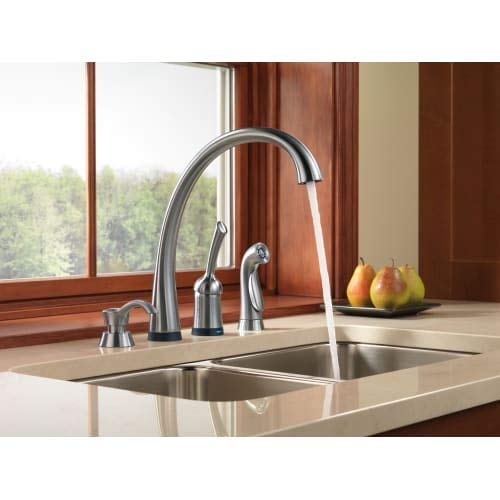 Stainless steel soap dispenser with cylindrical pump next to kitchen faucet on countertop.