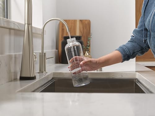 Stainless steel beverage faucet with curved spout positioned above kitchen sink, dispensing water into glass.