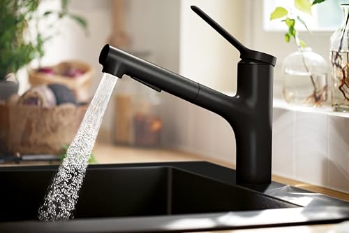 Matte black kitchen faucet with pull-out spray head extended over sink, water flowing from spout.