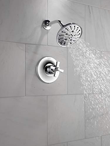 Chrome tub filler with round showerhead and single-handle valve mounted on white tile wall with water flowing.
