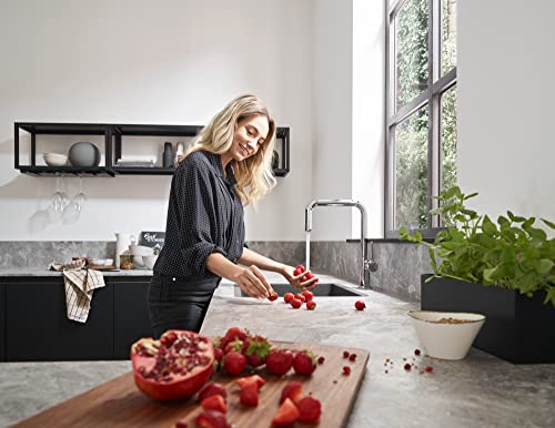 Brushed black chrome U-style kitchen faucet with single spray head mounted above gray countertop, woman rinsing red peppers.