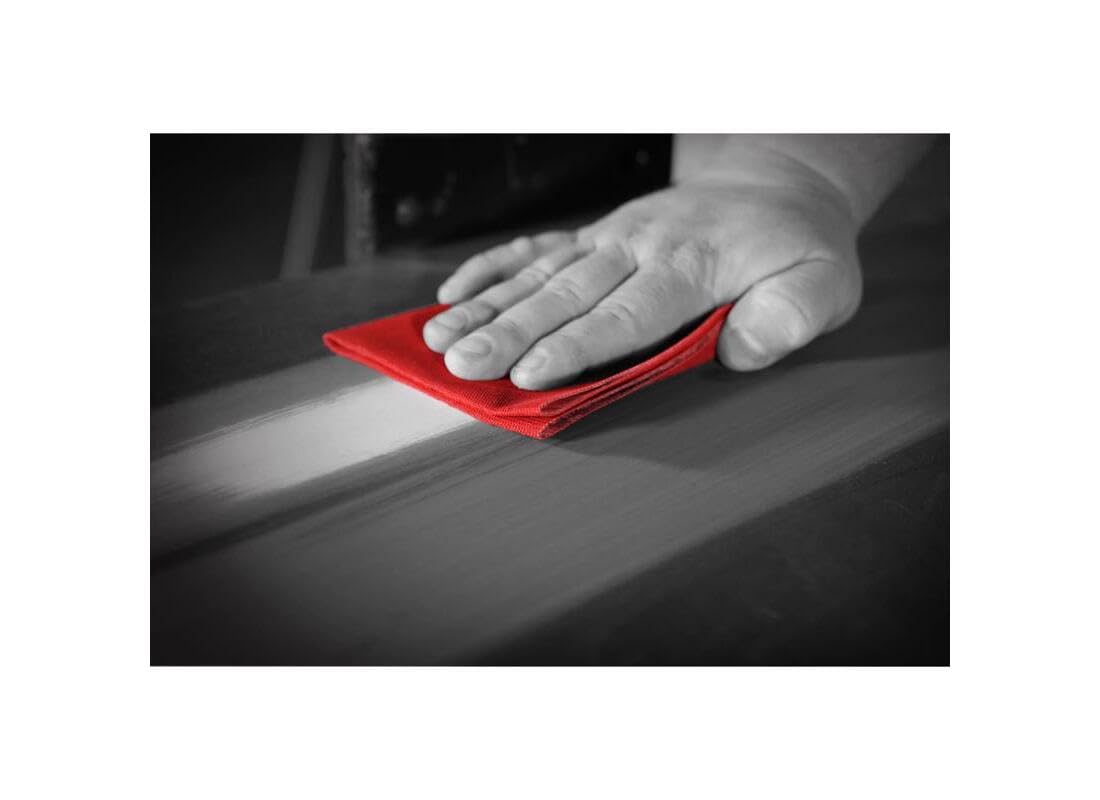 Hand using red sanding sheet on wooden surface during finishing work.